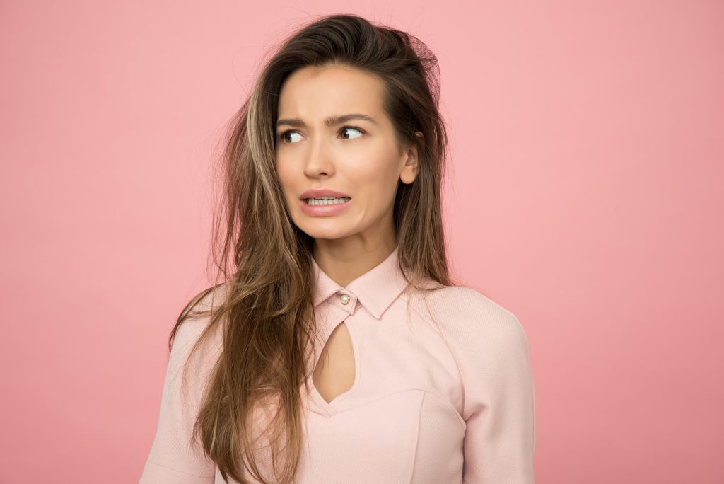 beautiful woman with brown hair grimacing and looking away to the left in a light pink top against a dark pink background